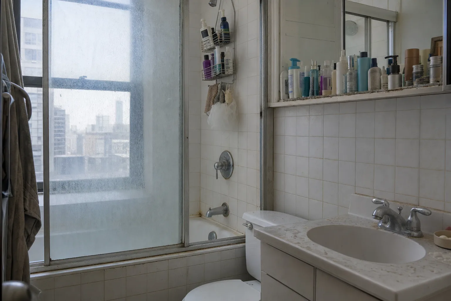 Bathroom with hard-water scale clouding the shower glass and a crowded shelf